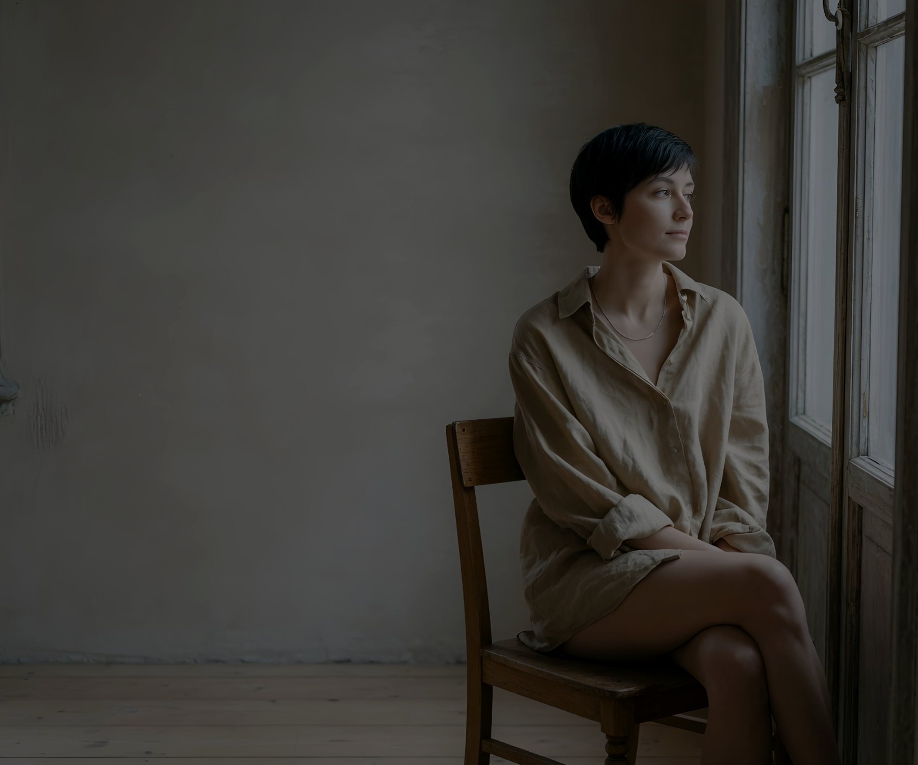 Natural-light portrait of a woman in an oat linen shirt sitting by a tall window.